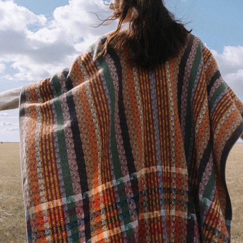 Back view of Tibetan geometric striped shawl showing vertical and horizontal woven texture pattern on grassland