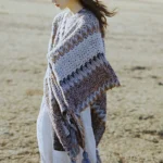 Tibetan striped knit shawl with tassel details worn on left side, showcasing gray-brown geometric weave pattern in outdoor grassland setting