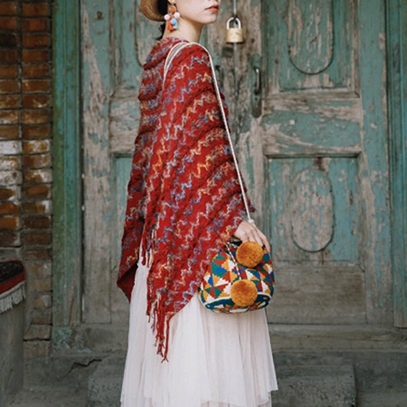 Ethnic tibetan striped tassel shawl with colorful woven pattern worn as side wrap with crossbody bag in front of retro wooden door