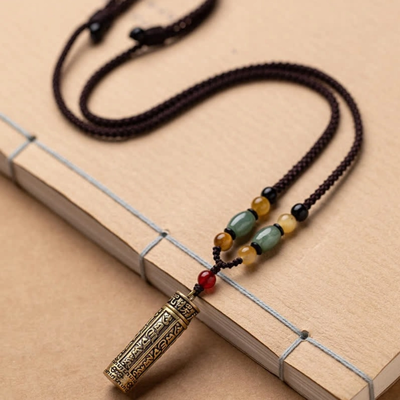 Handmade Tibetan sutra pendant necklace with braided rope and stone beads positioned with spiritual book on brown background