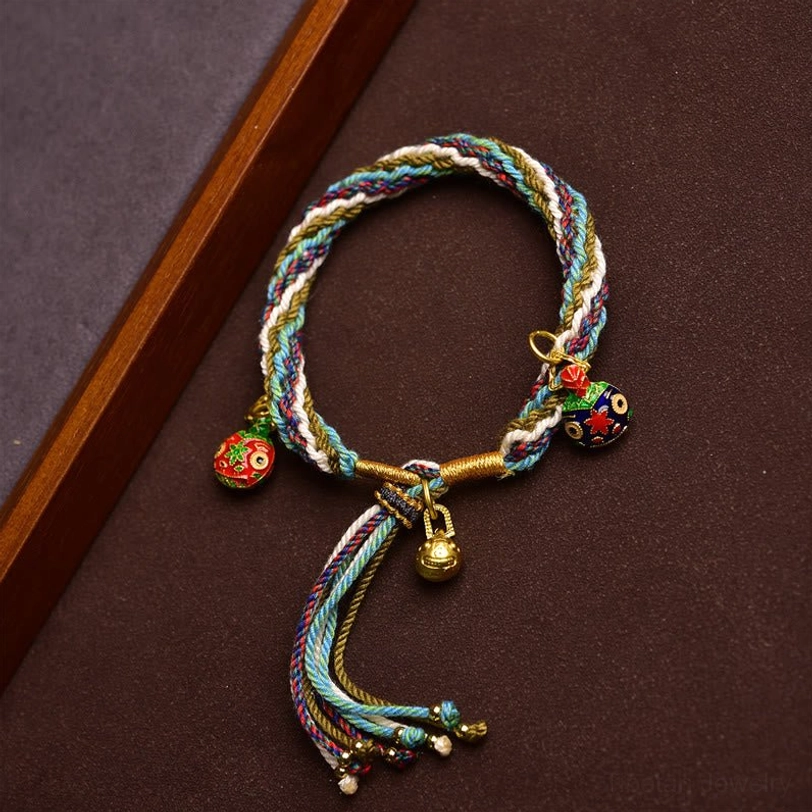Alternate angle of handmade Tibetan gold swallowing beast family bracelet with braided rope and protective enamel pendants
