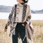 Tibetan geometric tassel shawl with ethnic tribal prints worn as a front poncho style wrap in lakeside outdoor grassland setting