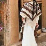 Tibetan geometric knit tassel shawl worn on shoulders, brown and beige striped pattern, rear full-body view against vintage wooden doorway