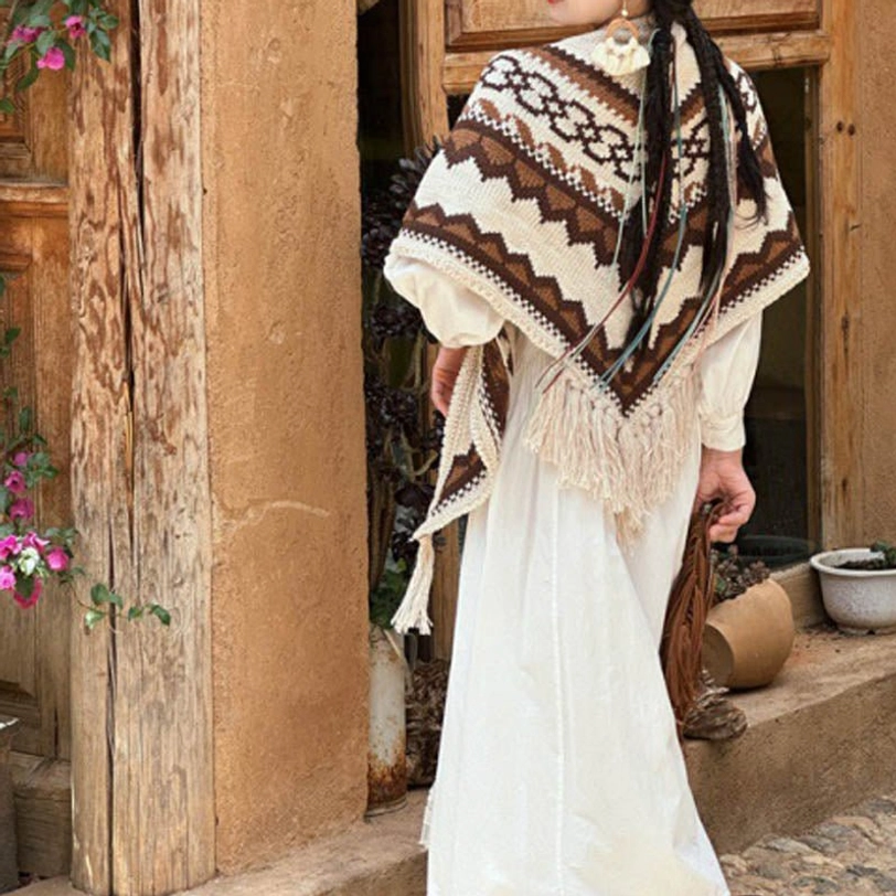 Tibetan geometric knit tassel shawl worn on shoulders, brown and beige striped pattern, rear full-body view against vintage wooden doorway