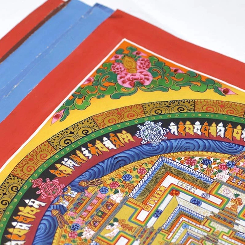 Close-up side view of hand-painted thangka border showing stacked colored canvas edges with fine Buddhist script and floral motifs
