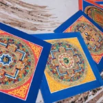 Tibetan handmade square mandala thangka with blue and red silk borders, featuring colorful gilt religious patterns and geometric designs