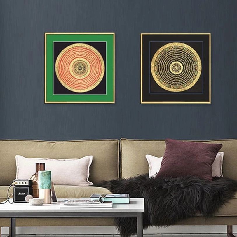 Two paired Tibetan mandala thangka paintings hung on dark grey wall above modern sofa with green and black decorative frames