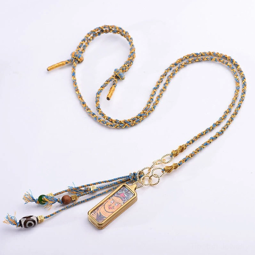 Tibetan deity thangka necklace overhead flat lay with blue-gold woven chain and metal links on white