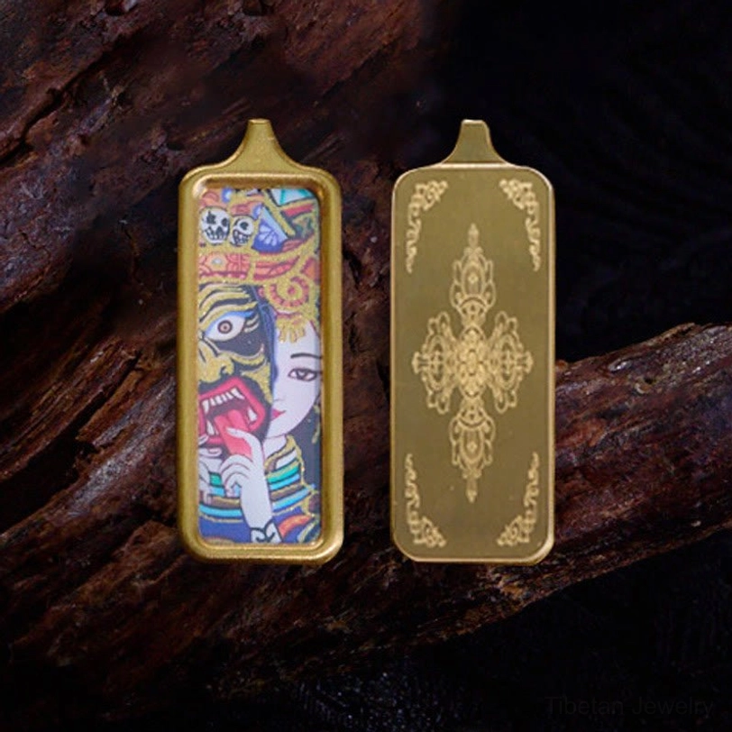 Double-sided Tibetan thangka hand-painted pendant with gold metal frame and vajra engraving, flat lay view on dark wood background