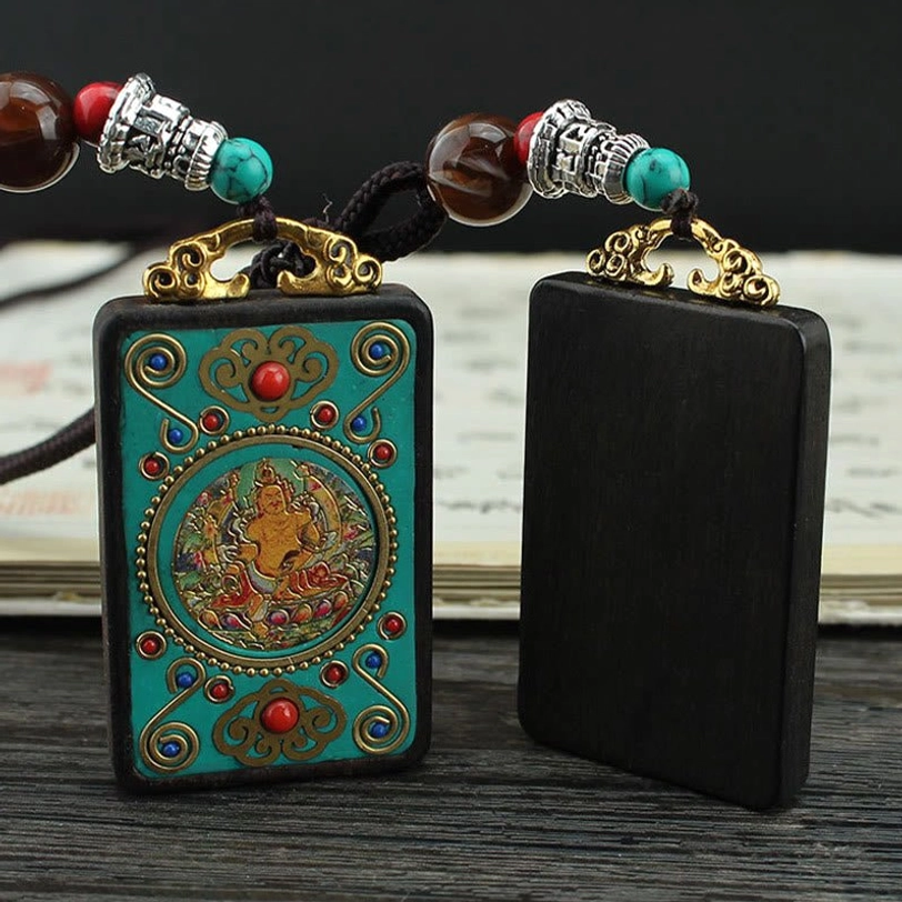Tibetan thangka pendant next to blank ebony wood pendant showing detailed Buddha artwork and natural wood craftsmanship on wooden backdrop