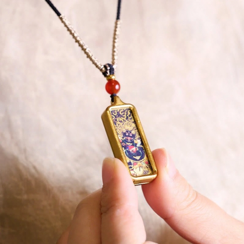 Hand-held Tibetan thangka hand-painted pendant with wrathful deity artwork in gold metal frame, displayed in first-person perspective