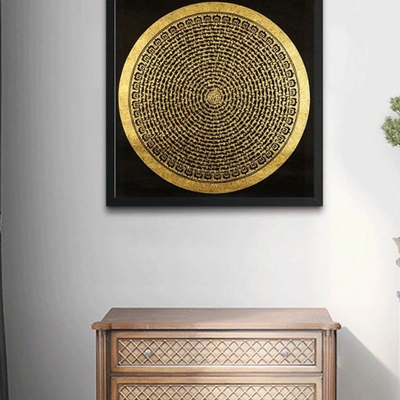 Wall-mounted round Tibetan mandala thangka with black frame and gold-on-black design above wooden cabinet
