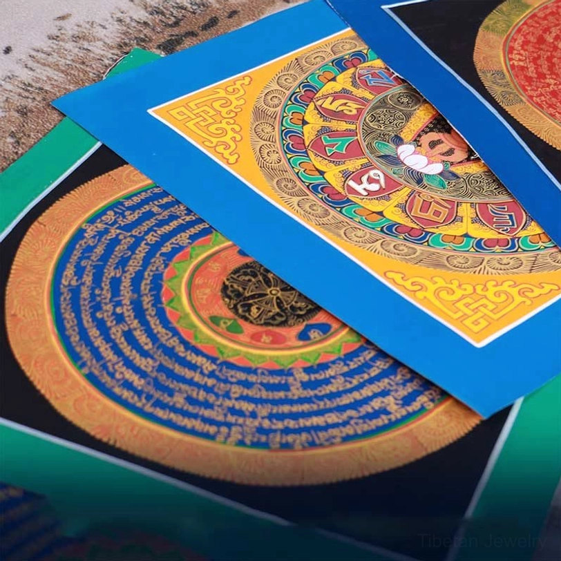 Set of stacked Tibetan thangka paintings displaying gilt mandala designs with blue and red silk borders