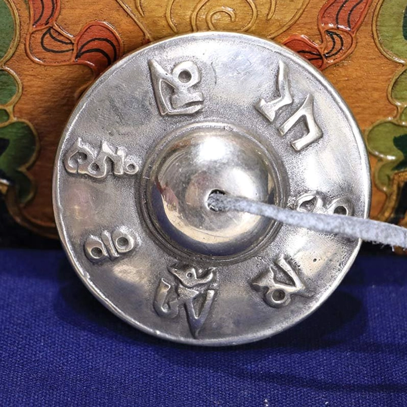 Single Tibetan tingsha bell om mani padme hum six true words white copper leather tether embossed detail wooden background