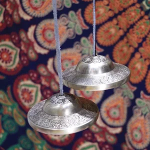 Hanging Tibetan tingsha cymbals front flat display ethnic fabric background polished brass