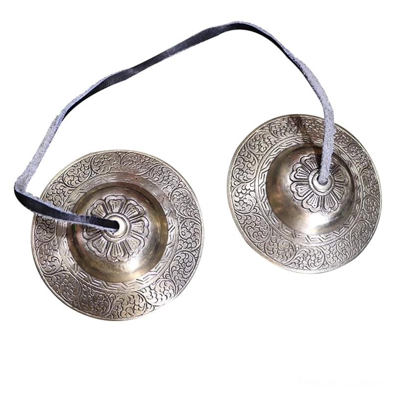 Tibetan tingsha brass bells pair angled flat view wooden table detailed floral center engravings