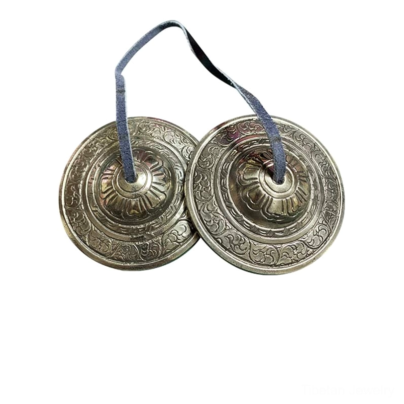 Pair of Tibetan tingsha bells top-down flat lay plain light background engraved floral leather straps