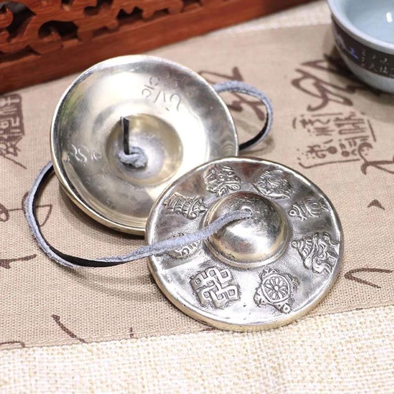 Tibetan tingsha bells pair white copper six true words mantra engraved leather strap overhead view calligraphy cloth