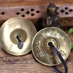 Tibetan tingsha cymbals pair with dragon and mantra engraving on wooden table with Buddhist figurine