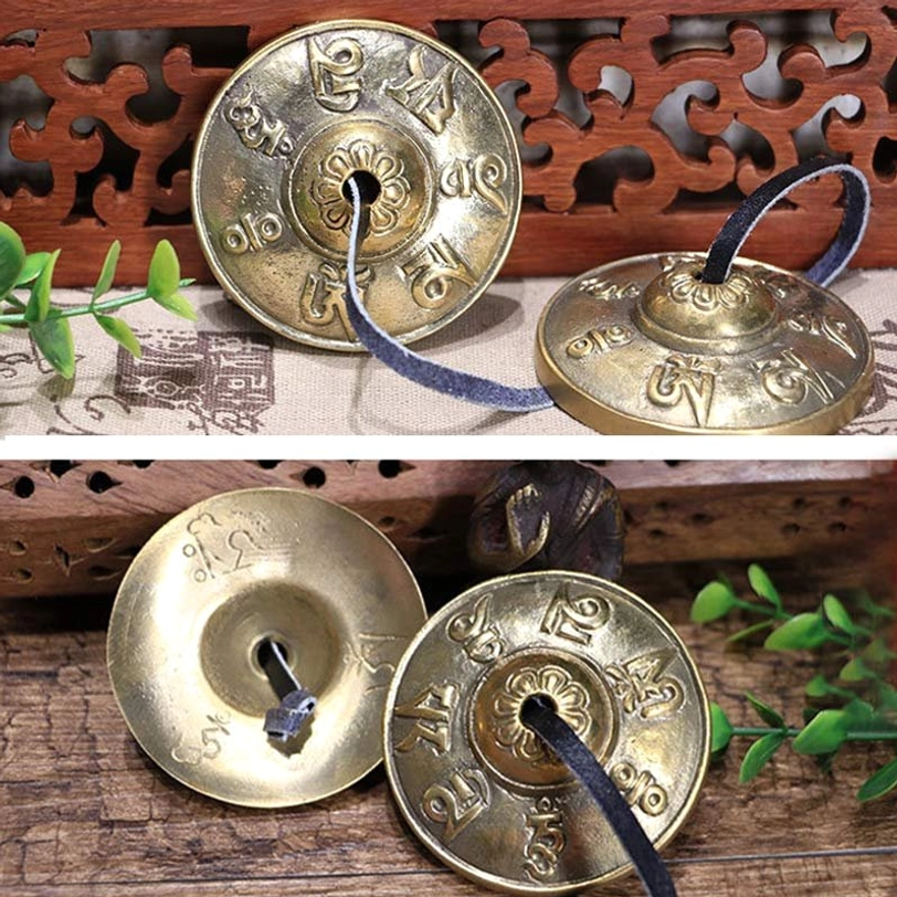 Flat lay overhead of brass tingsha cymbals on carved wood backdrop with green plants decoration