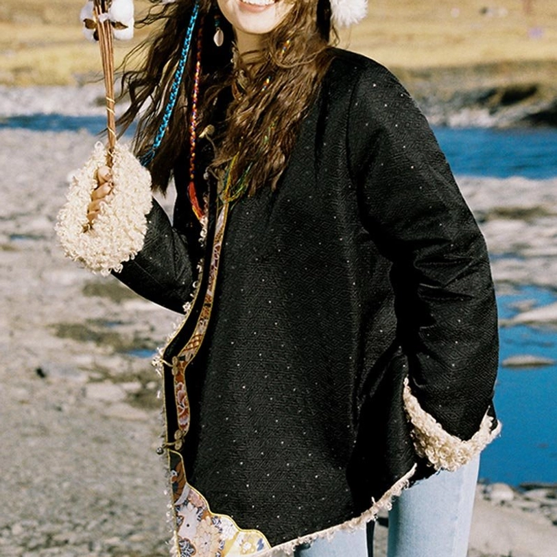 Side view of model wearing Tibetan ethnic fleece top outdoors showing ethnic trim and fuzzy cuffs with hand in pocket