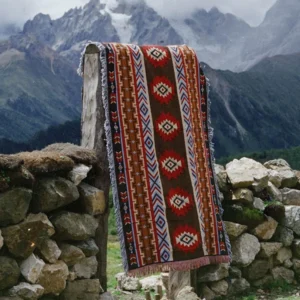 Ethnic Tibetan blanket hanging on stone wall outdoor showing southwestern geometric patterns dark brown base with red blue accents