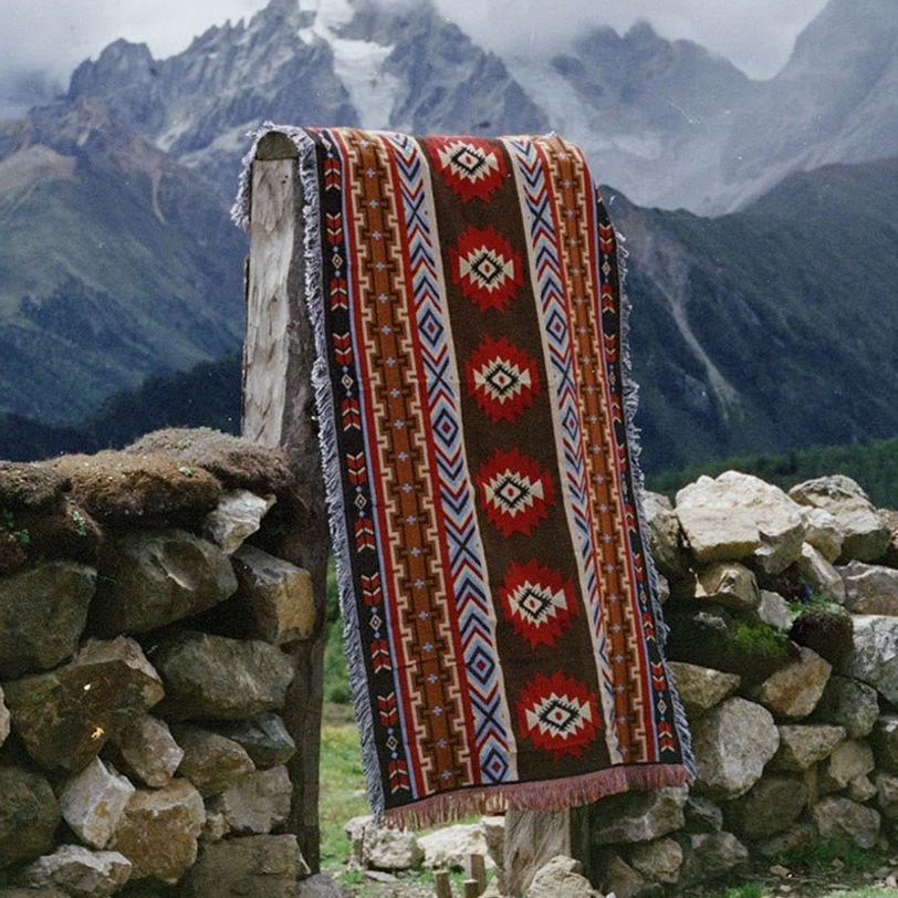 Ethnic Tibetan blanket hanging on stone wall outdoor showing southwestern geometric patterns dark brown base with red blue accents