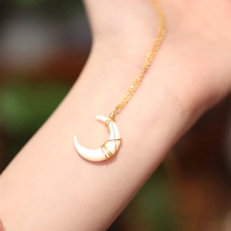 Crescent moon Tridacna necklace worn on wrist showing side profile of white shell pendant with gold chain