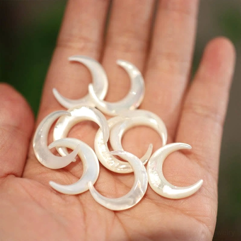 Loose Tridacna crescent shell charms in hand showing multiple blank white iridescent pieces for jewelry making