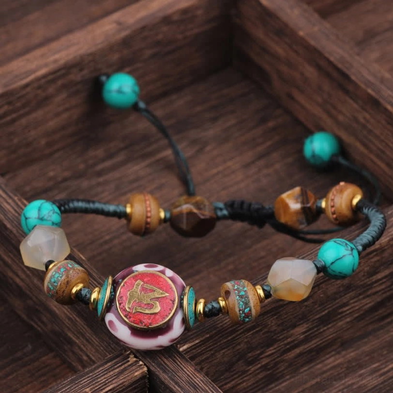 Tibetan turquoise amber braided rope healing bracelet with carved gemstone bead on dark wooden tray