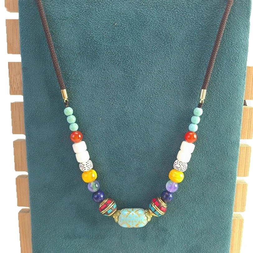 Tibetan turquoise beaded necklace with brown wax cord and gemstone bead set on teal suede background