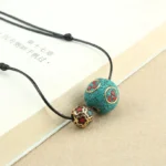 Tibetan turquoise double bead necklace with antique enamel details displayed on book with natural light, showing crack-textured stone