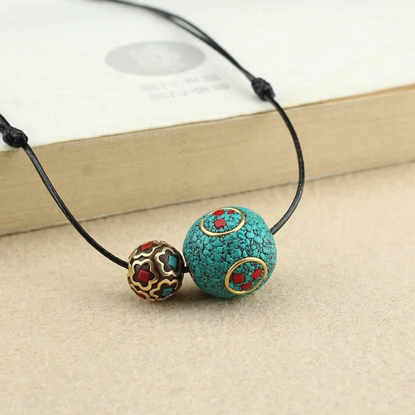 Tibetan double bead necklace pendant displayed on book edge showing both beads and decorative elements in clear view