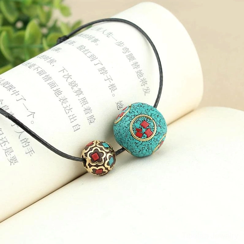 Tibetan turquoise double bead pendant with clear ethnic pattern details displayed on book with natural green plant background
