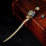 Tibetan turquoise agate hairpin with bronze carved shaft and colorful gem beads, flat lay on dark fabric and wooden backdrop