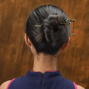 Woman wearing Tibetan turquoise hairpin securing low bun hairstyle from back view, indoor warm lighting