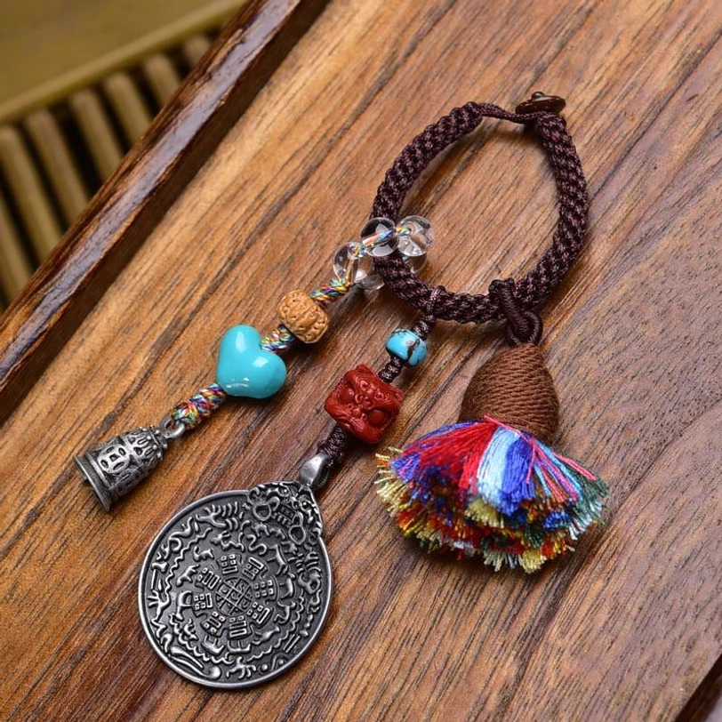 Turquoise heart Tibetan amulet keychain with dual tassels, brown braided rope, silver Bagua plaque on natural wood background