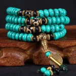 Tibetan 108 turquoise mala beads with three-eye dzi beads and antique gold guru bead on wooden display