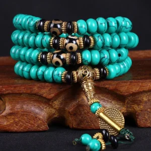 Tibetan 108 turquoise mala beads with three-eye dzi beads and antique gold guru bead on wooden display