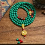Tibetan 108 turquoise mala beads necklace with dzi bead spacers on wooden surface, showing authentic prayer beads with decorative tassel