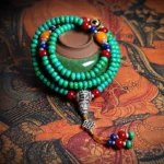 108 Tibetan turquoise mala bracelet with hand-painted dzi bead displayed on traditional Tibetan tapestry, featuring teal turquoise beads, colorful accent stones, silver guru bead, and decorative tassel charm