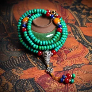 108 Tibetan turquoise mala bracelet with hand-painted dzi bead displayed on traditional Tibetan tapestry, featuring teal turquoise beads, colorful accent stones, silver guru bead, and decorative tassel charm