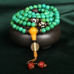 Tibetan turquoise 108 mala necklace with three-eye Dzi beads and amber guru bead, displayed on dark velvet with wooden base, top-down view