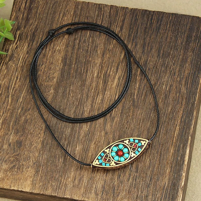 Compact Tibetan turquoise pendant necklace with colorful ethnic enamel, coiled on dark wooden surface
