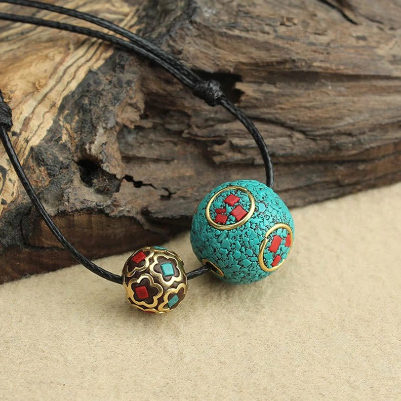 Tibetan turquoise protection necklace with black wax rope showing red-gold inlay details on natural tabletop