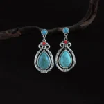 Tibetan turquoise teardrop dangle earrings with silver filigree, hanging on wooden twig, front view