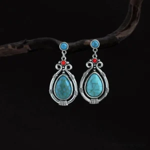Tibetan turquoise teardrop dangle earrings with silver filigree, hanging on wooden twig, front view