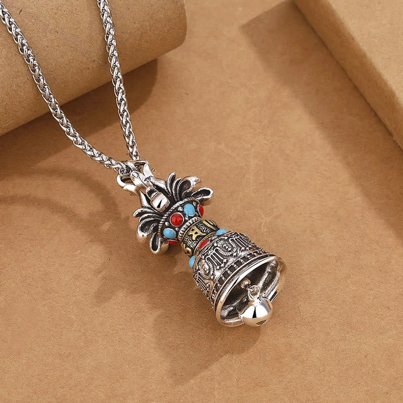 Handmade Tibetan Vajra Bell pendant with swinging silver bead detail at bottom, vintage silver alloy material, shown from right front angle on kraft paper background