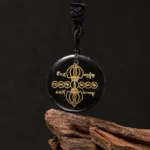 Black obsidian Vajra Dorje Tibetan necklace pendant with golden Sanskrit engraving and braided black rope, three-quarter view on wooden surface