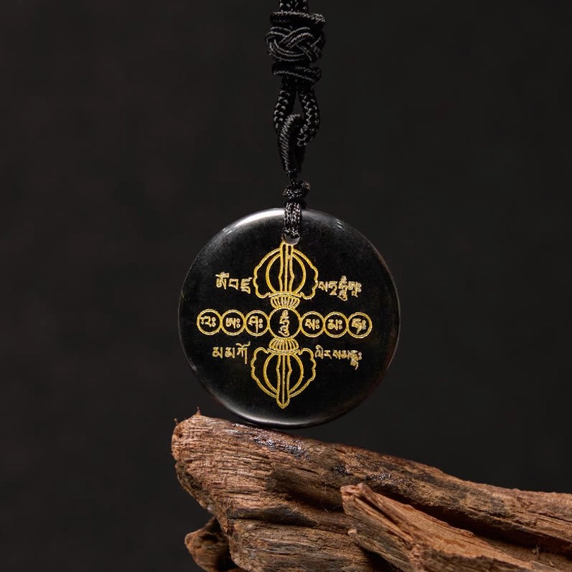 Black obsidian Vajra Dorje Tibetan necklace pendant with golden Sanskrit engraving and braided black rope, three-quarter view on wooden surface